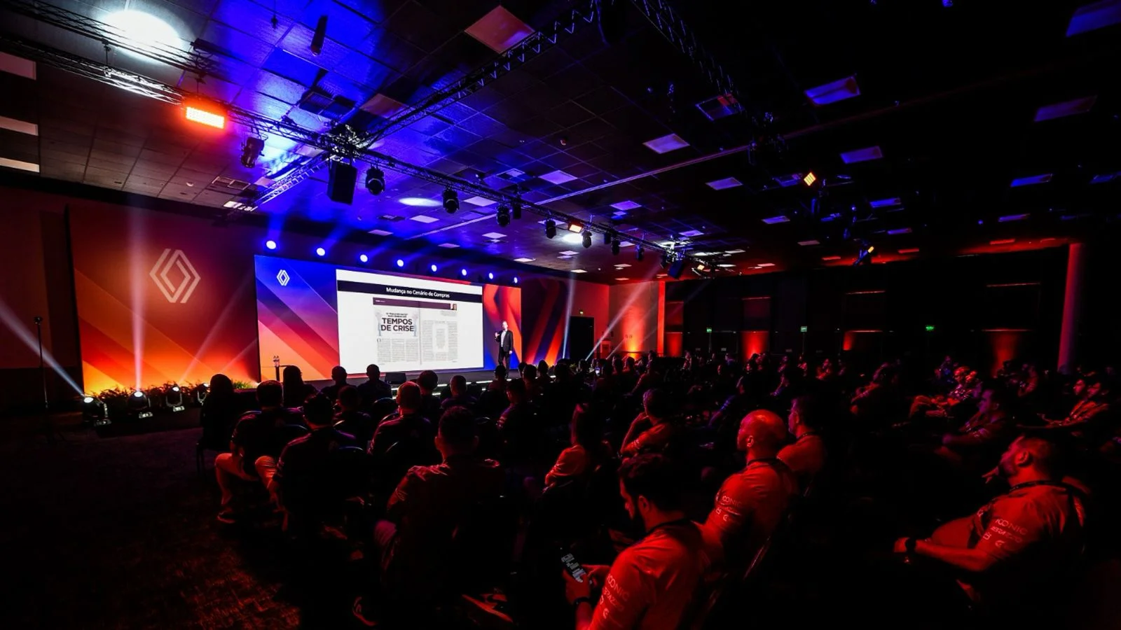 Palco de evento corporativo com plateia durante palestra do Prof. Alfredo Bravo